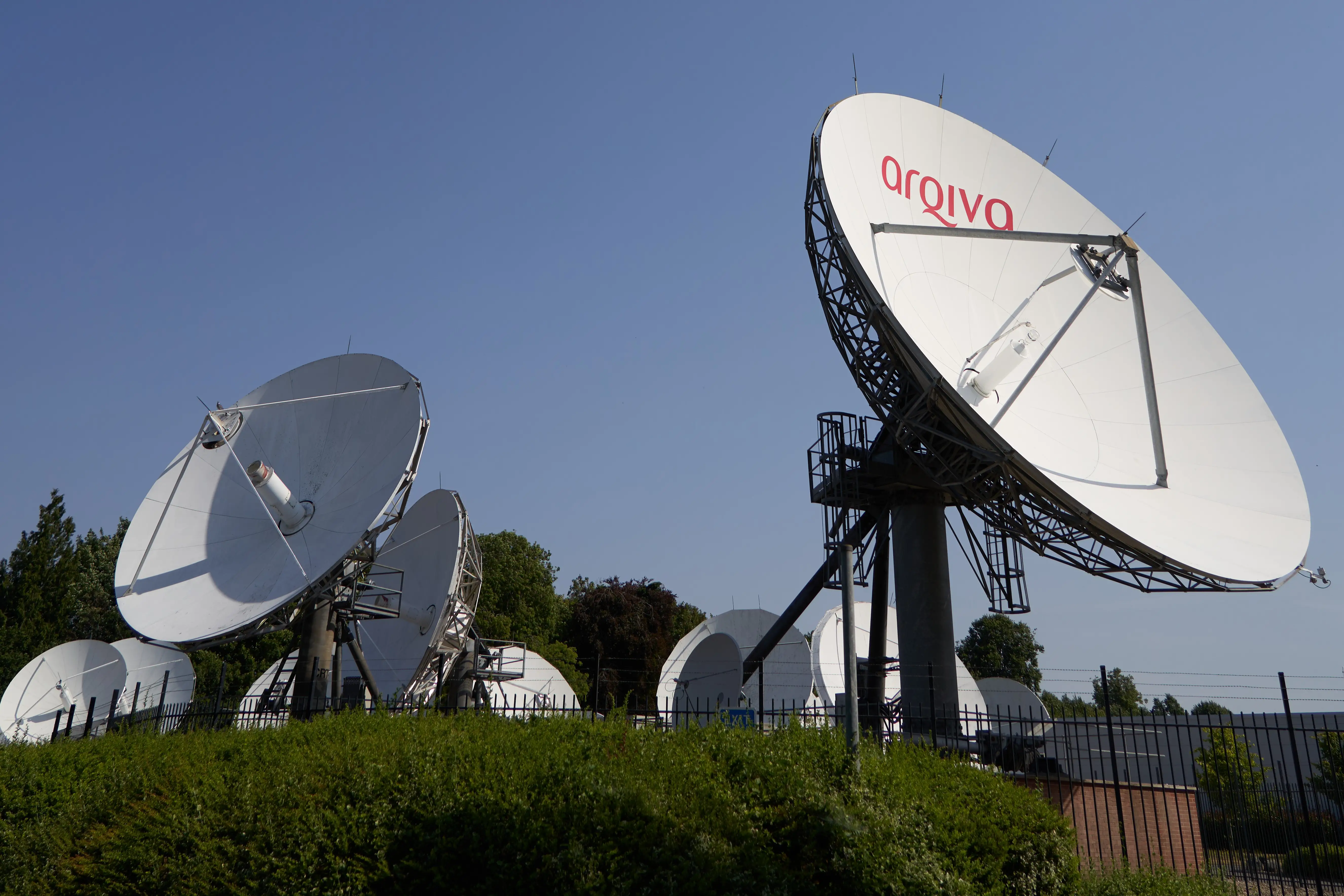 Ground station satellite dishes pointing to the sky. One dish has the words Arqiva visible on it in red lettering